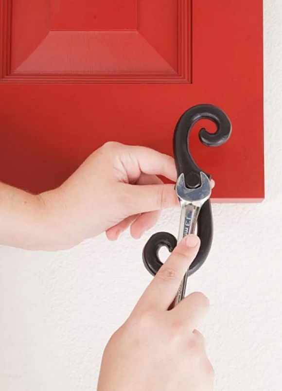 A person using a wrench on a decorative hook attached to a red door.