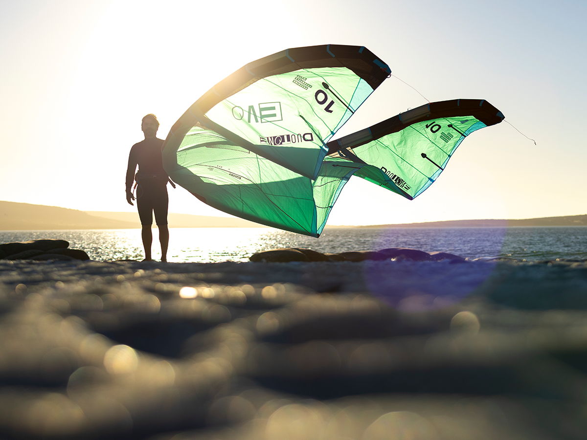 Person holding a kite on the beach against a bright sunset.
