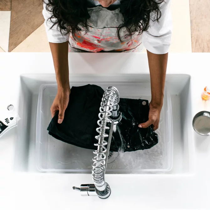 Person washing black clothing in a sink.