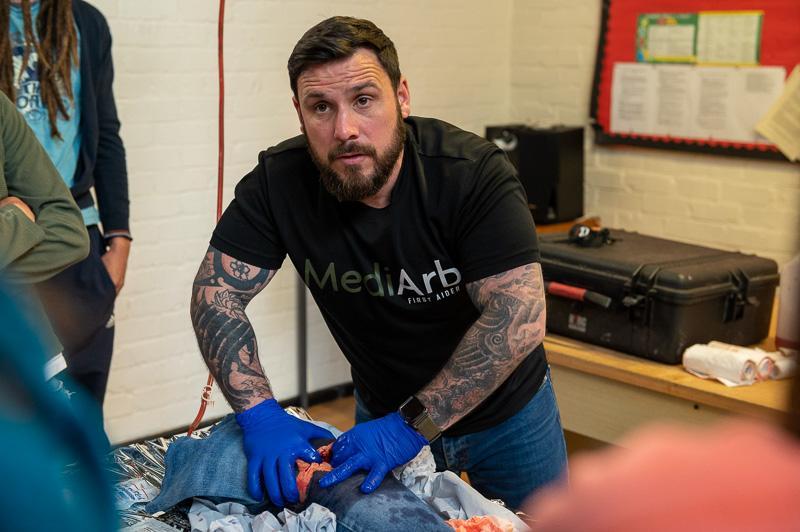 Man demonstrating a technique while wearing gloves, surrounded by onlookers.