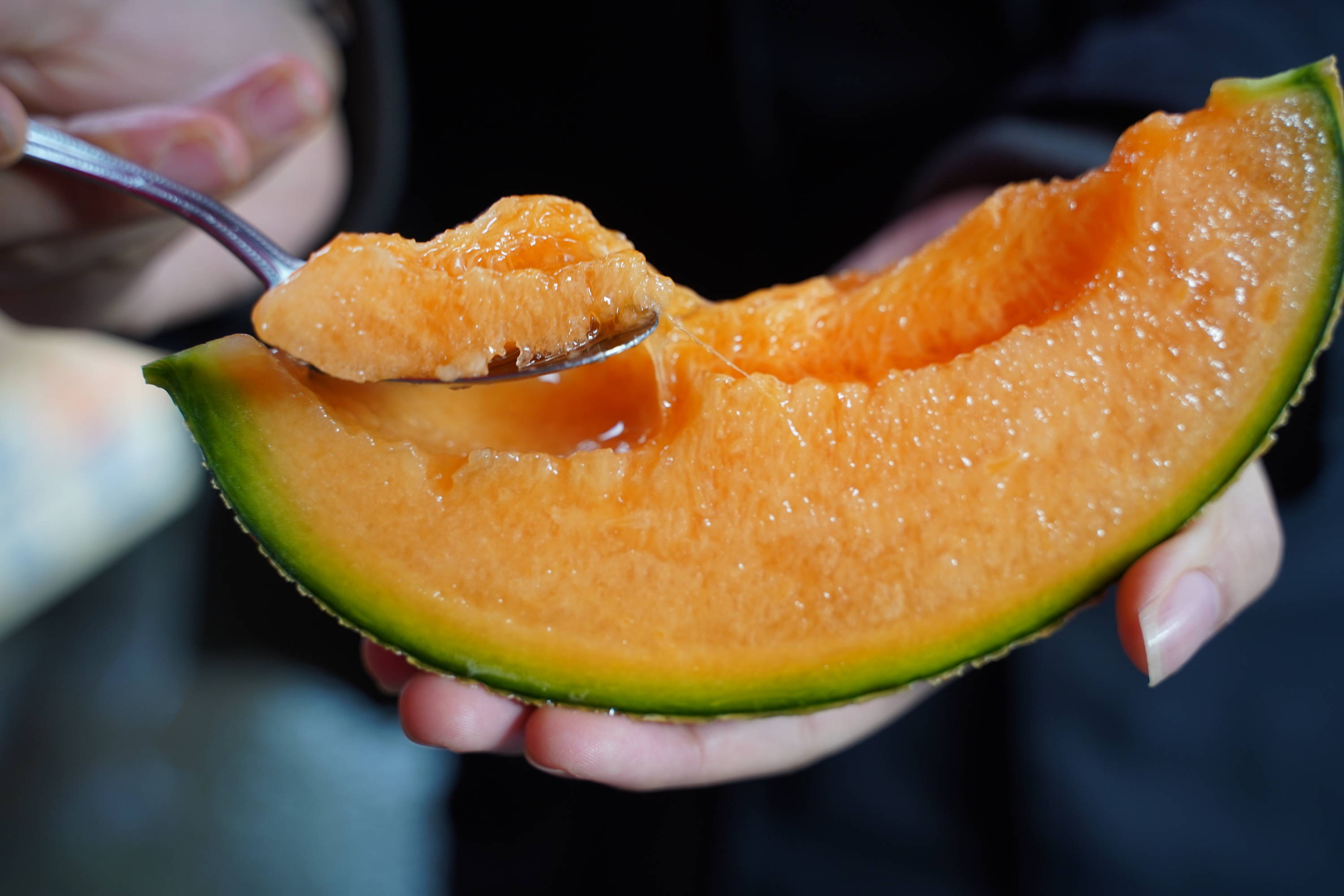 This is a picture of a slice of cantaloupe being spooned by a person.