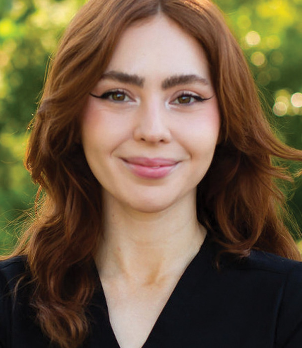 Smiling young woman with long brown hair against a green background.