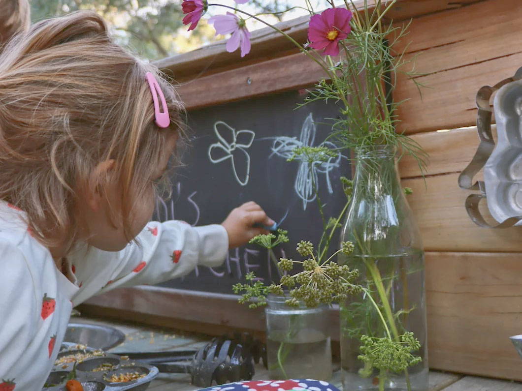 A girl drawing on a mud kitchen's black board