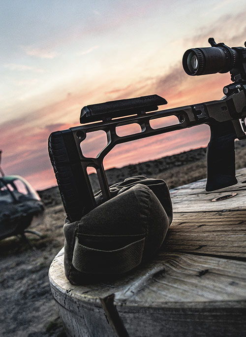 Rifle resting on a wooden surface with a sunset background.