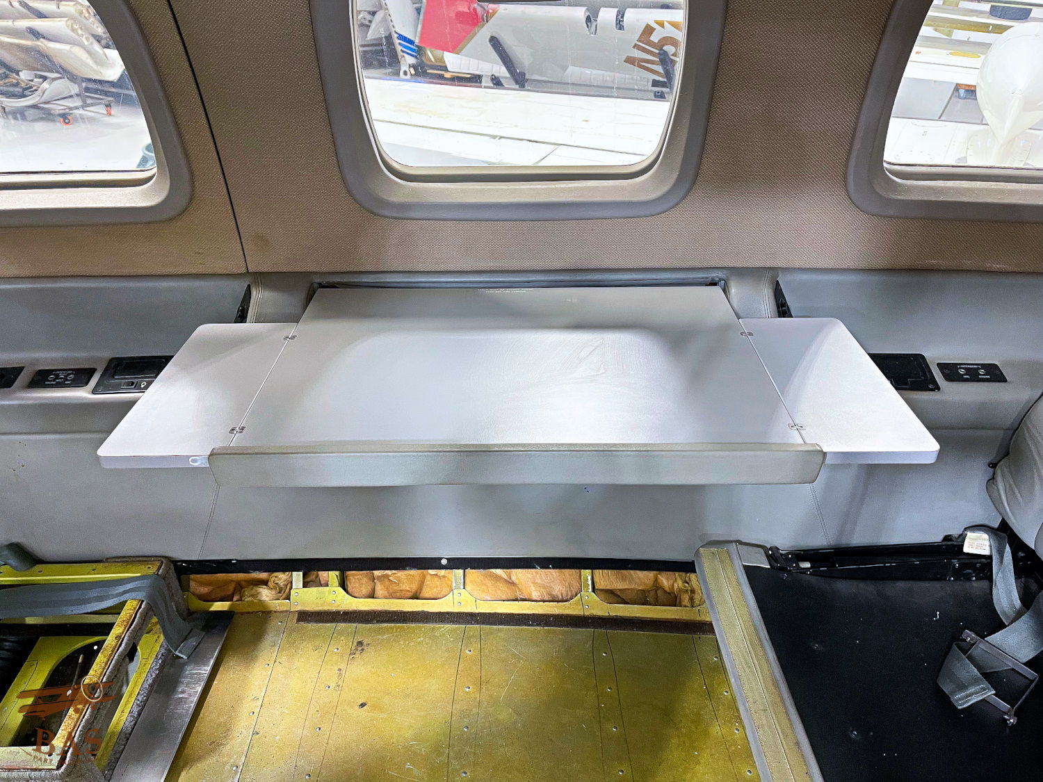 Interior view of an aircraft cabin with a metal shelf and windows.