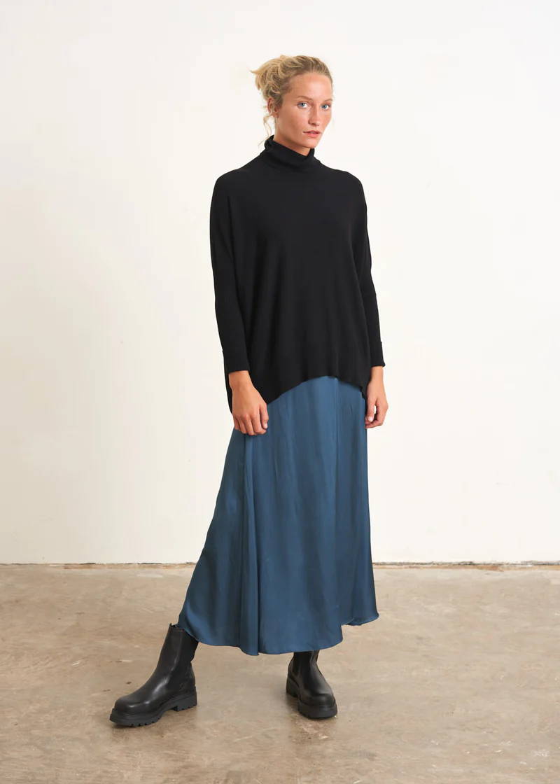 A model wearing a teal, satin maxi skirt with a black turtleneck jumper and black leather chelsea boots