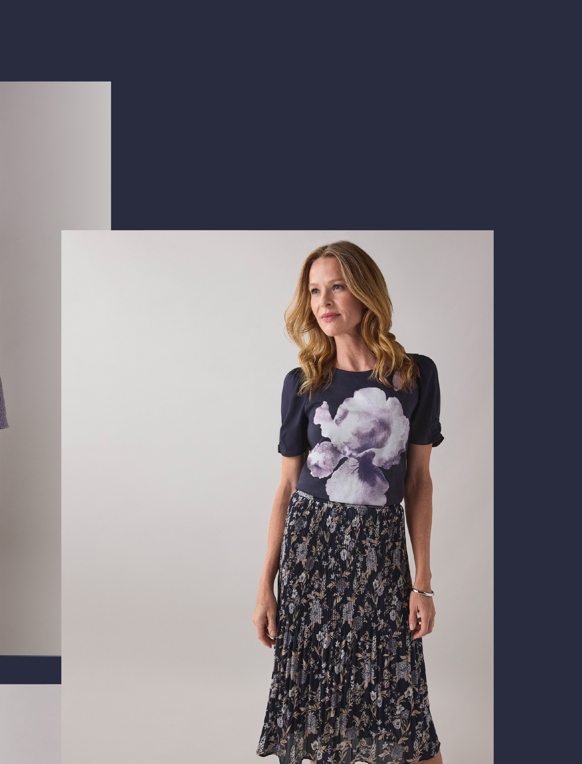 Woman wearing a floral shirt and patterned skirt, posing against a neutral background.