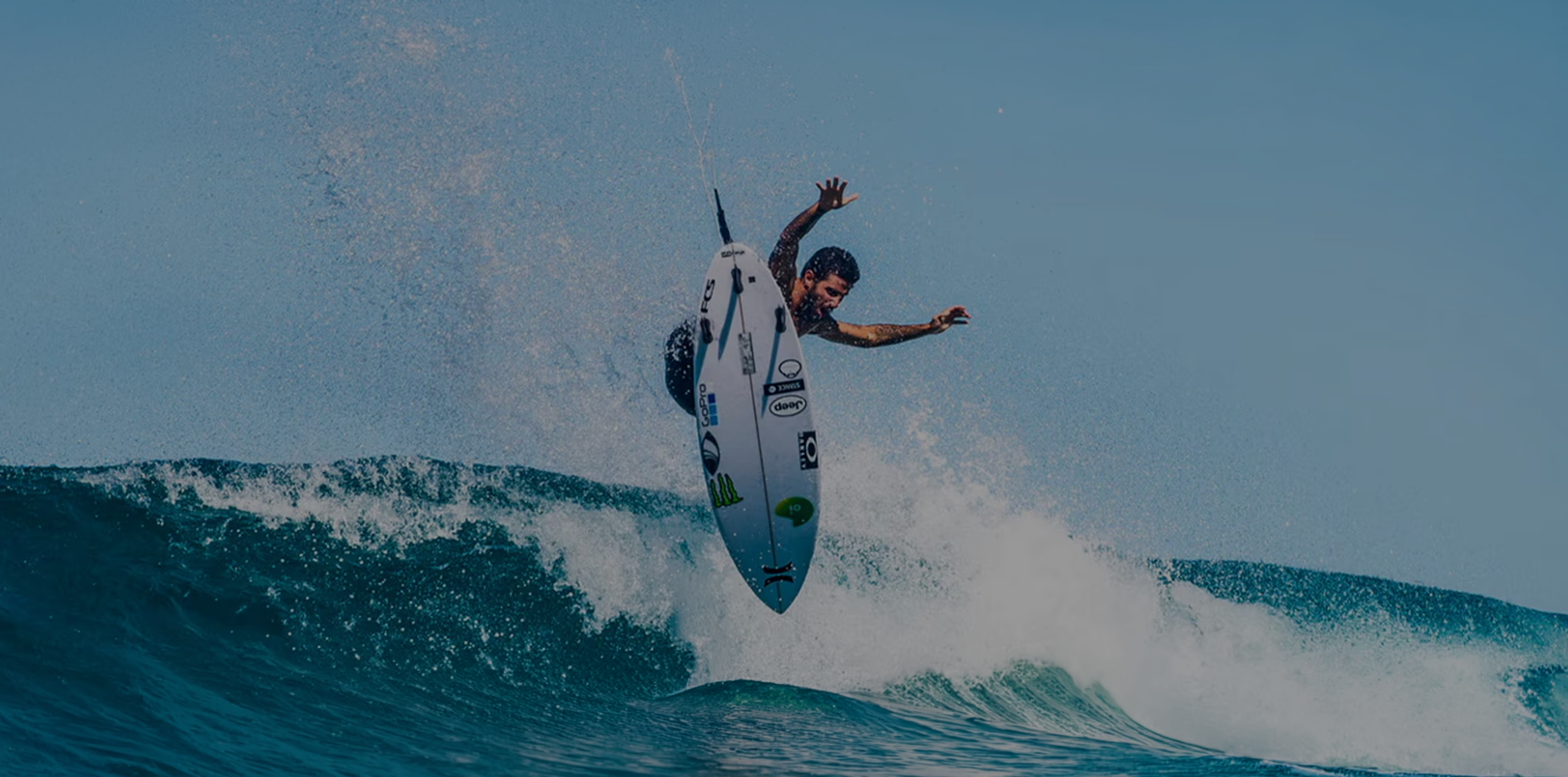 A surfer performing a trick on a wave under a clear blue sky.