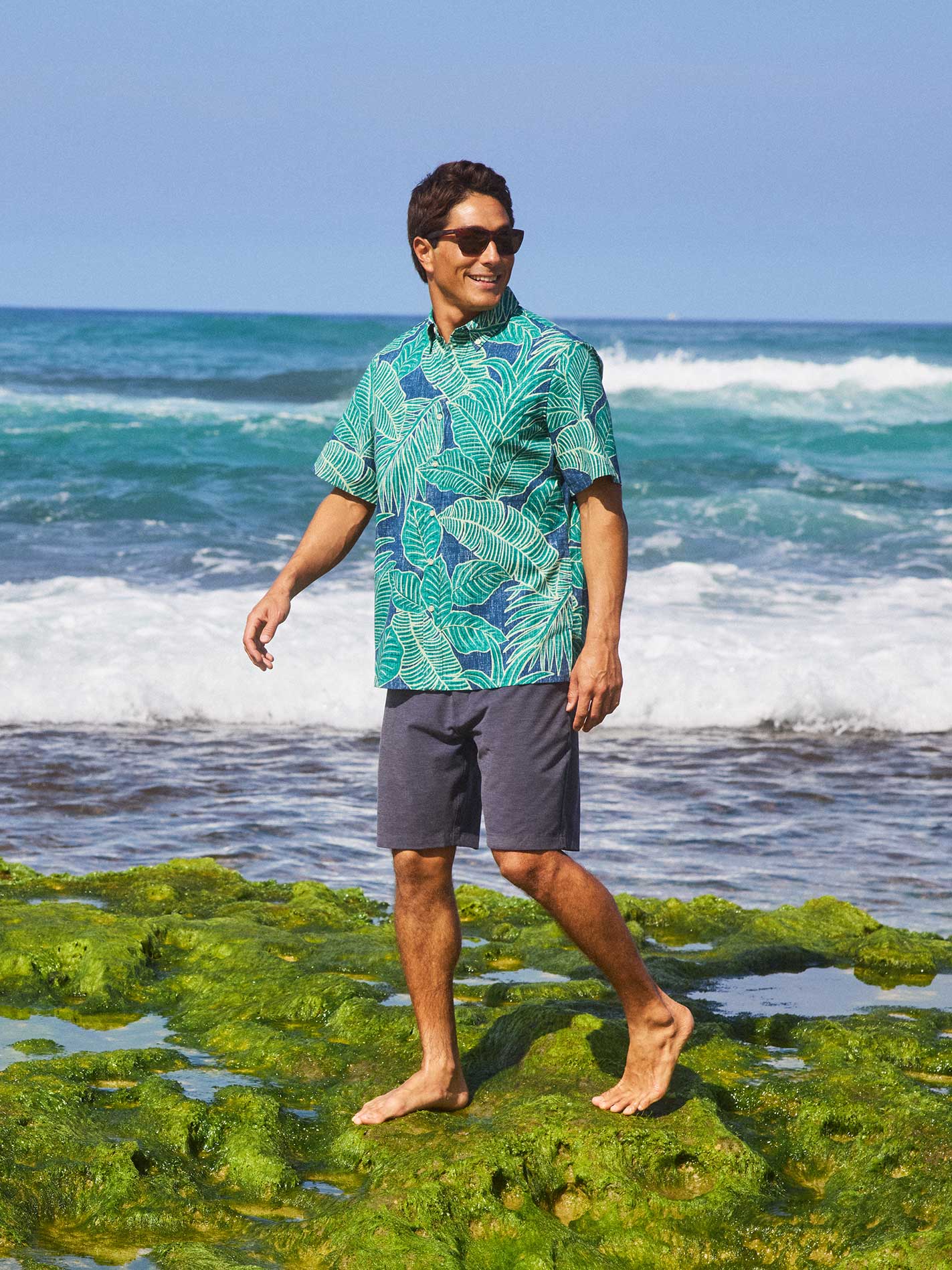 Person in a colorful shirt walking on rocks by the ocean.