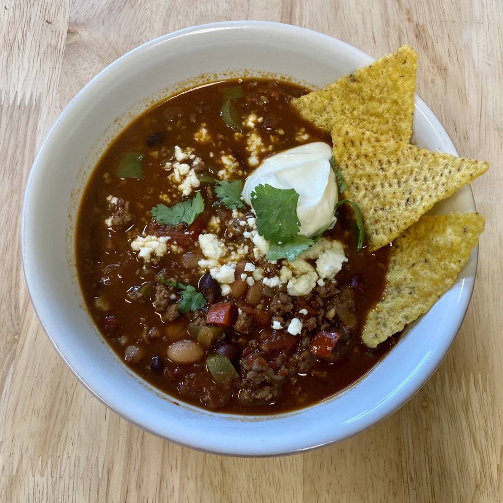 Bowl of Andrew's chili with dark chocolate topped with sour cream, cilantro and chps