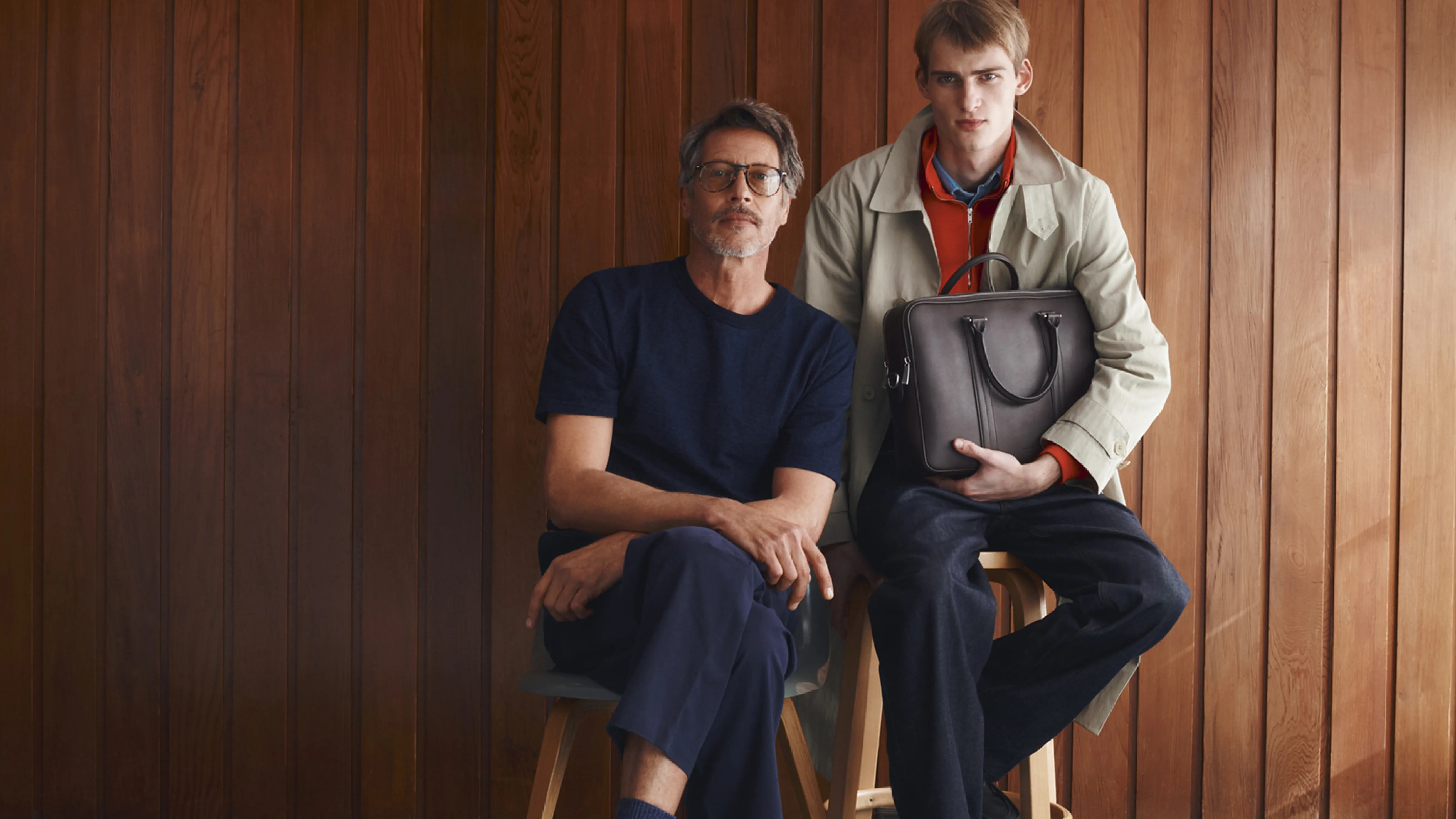 Two men posing together in front of a wooden wall.