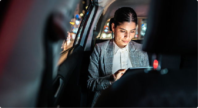 Woman using a tablet in the backseat of a car at night.