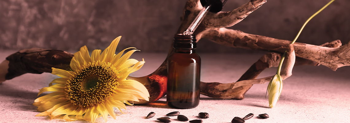 A brown glass bottle, sunflower, and natural elements on a surface.