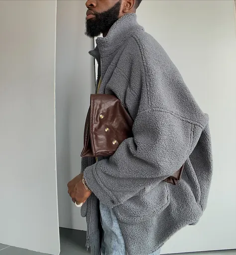 Person wearing a gray oversized jacket, holding a brown bag.