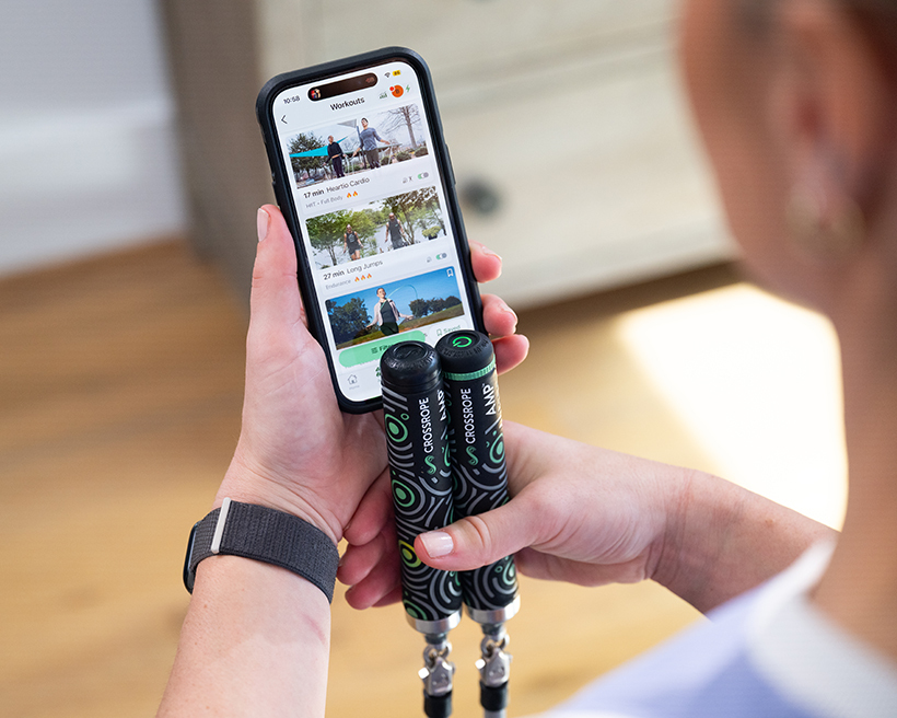 Person holding a smartphone and jump rope, viewing fitness app on screen.