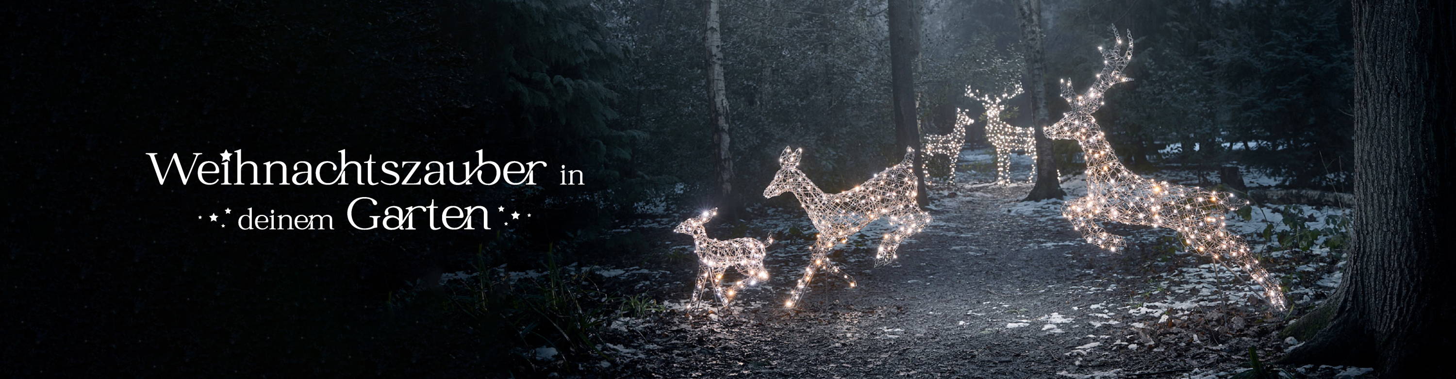 Drei LED Rentiere im Sprung  in einem winterlichen Wald, im Hintergrund zwei stehende Rentiere