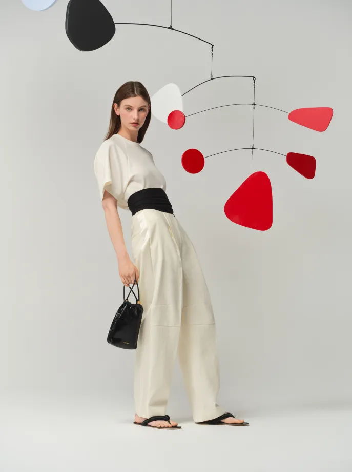 Model in stylish outfit posing with abstract mobile art in background.