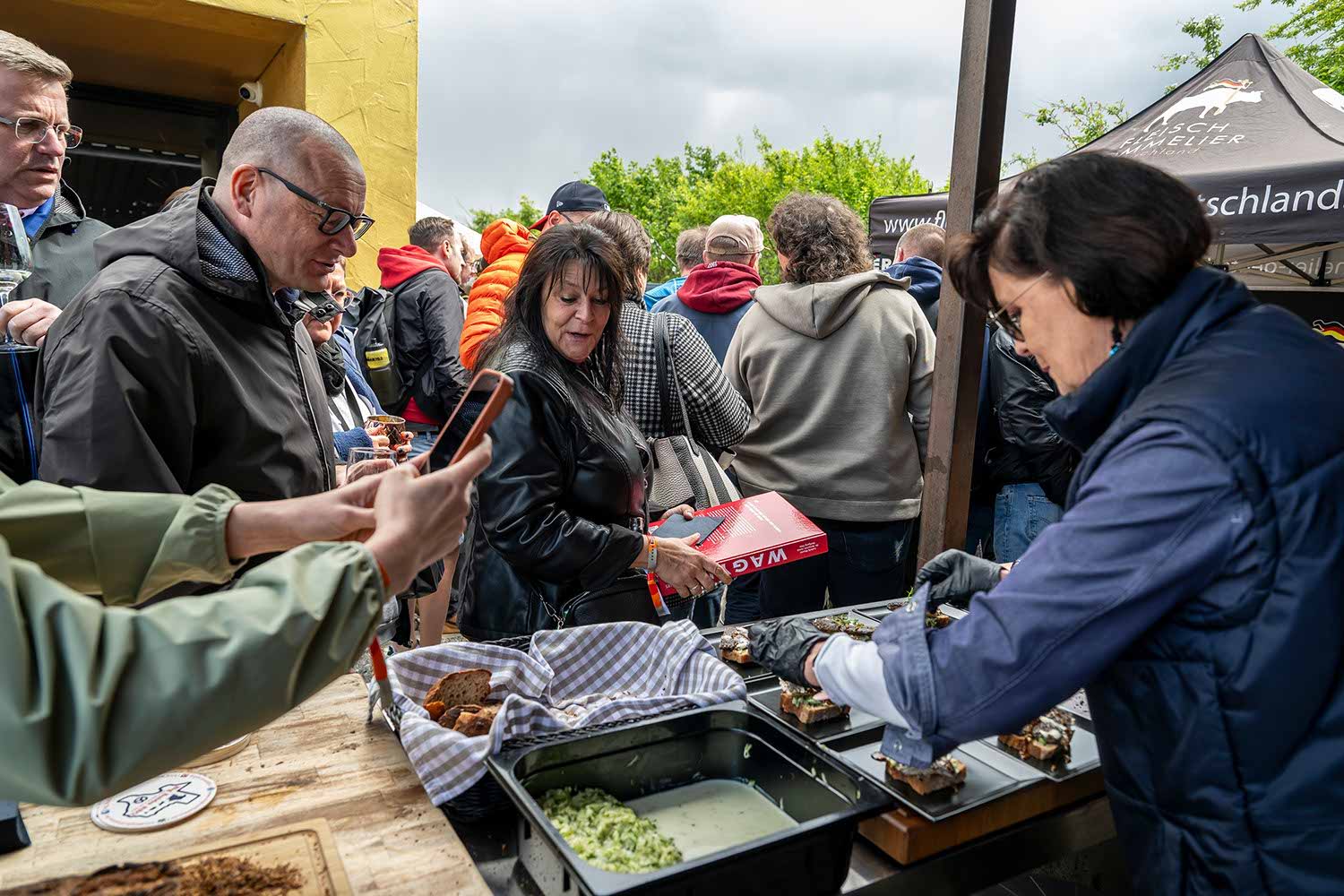 People at a food stall selecting and serving dishes outdoors.