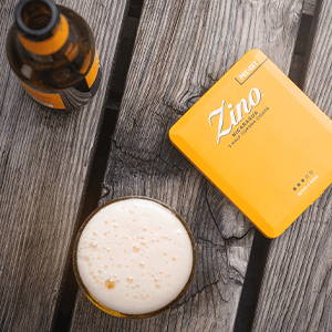 The yellow tin of Zino Nicaragua Half Corona cigars on a wooden table next to a pint of beer.