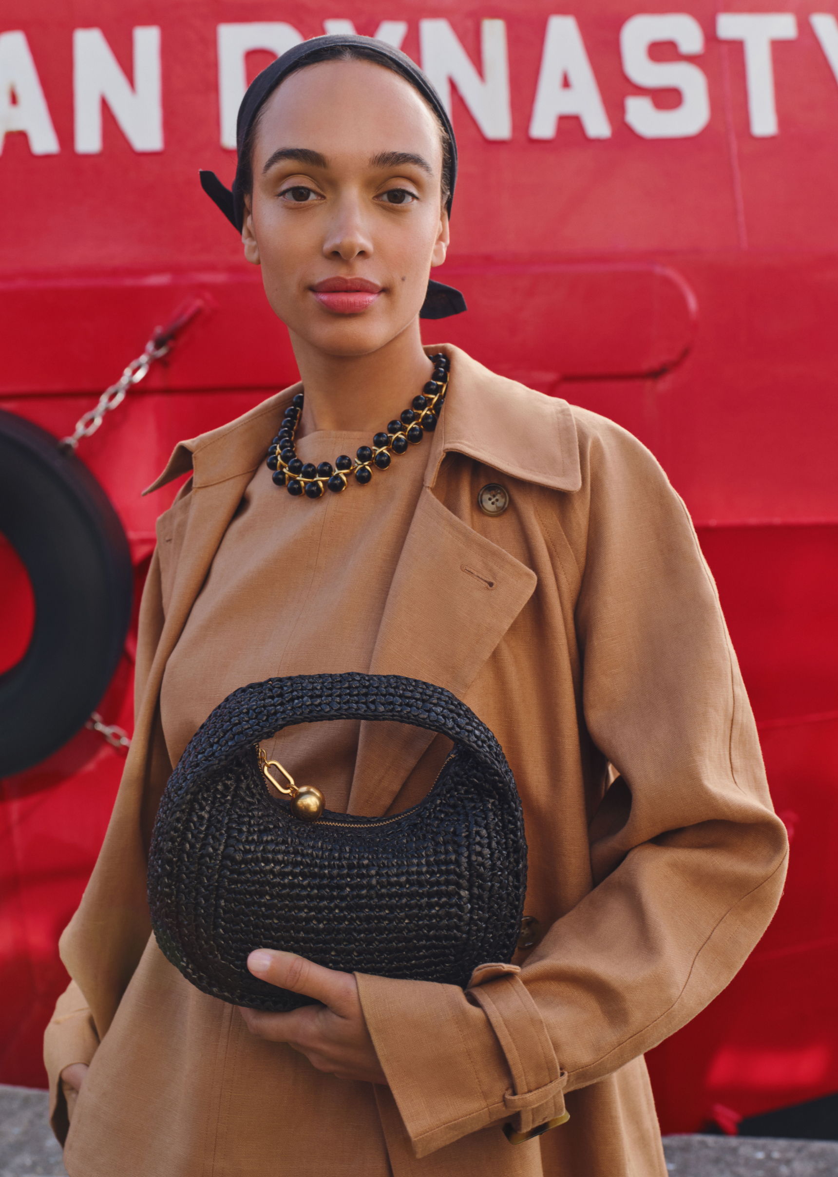 Person in a stylish outfit holding a black handbag against a red background.