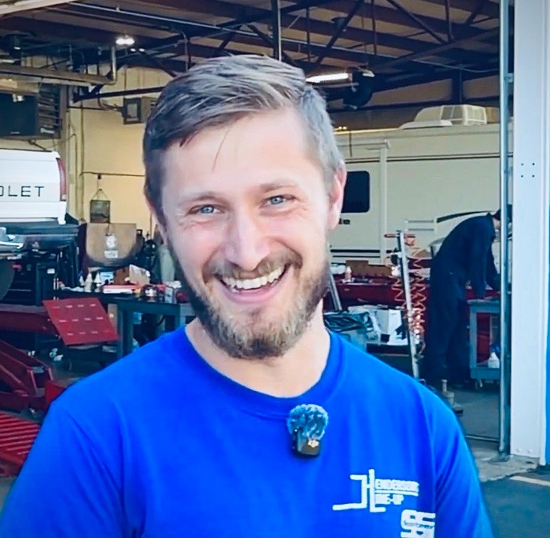 Smiling man in a blue shirt, standing in a workshop.