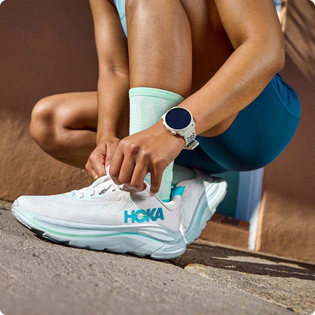Person tying HOKA shoes while wearing athletic attire and a watch.