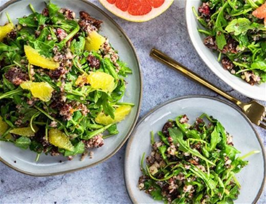 Three bowls of fresh salad with greens and citrus on a table.