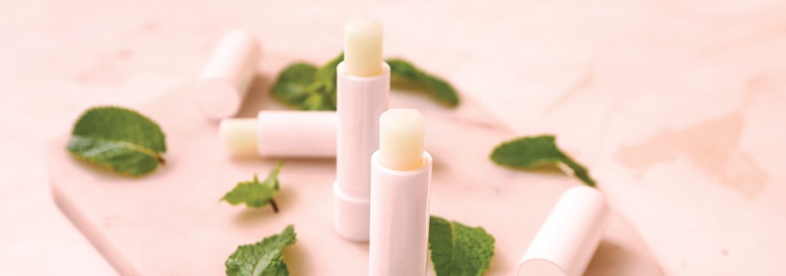 Lip balms arranged with green leaves on a light background.