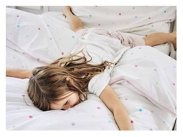 Young girl laying on top of confetti spot bedding