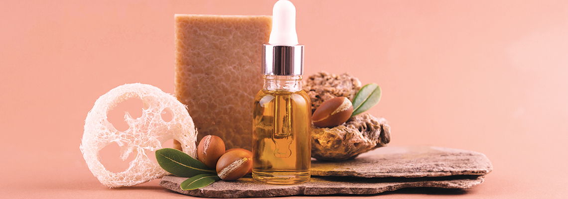 Bottle of oil, soap, and nuts on a light pink background.