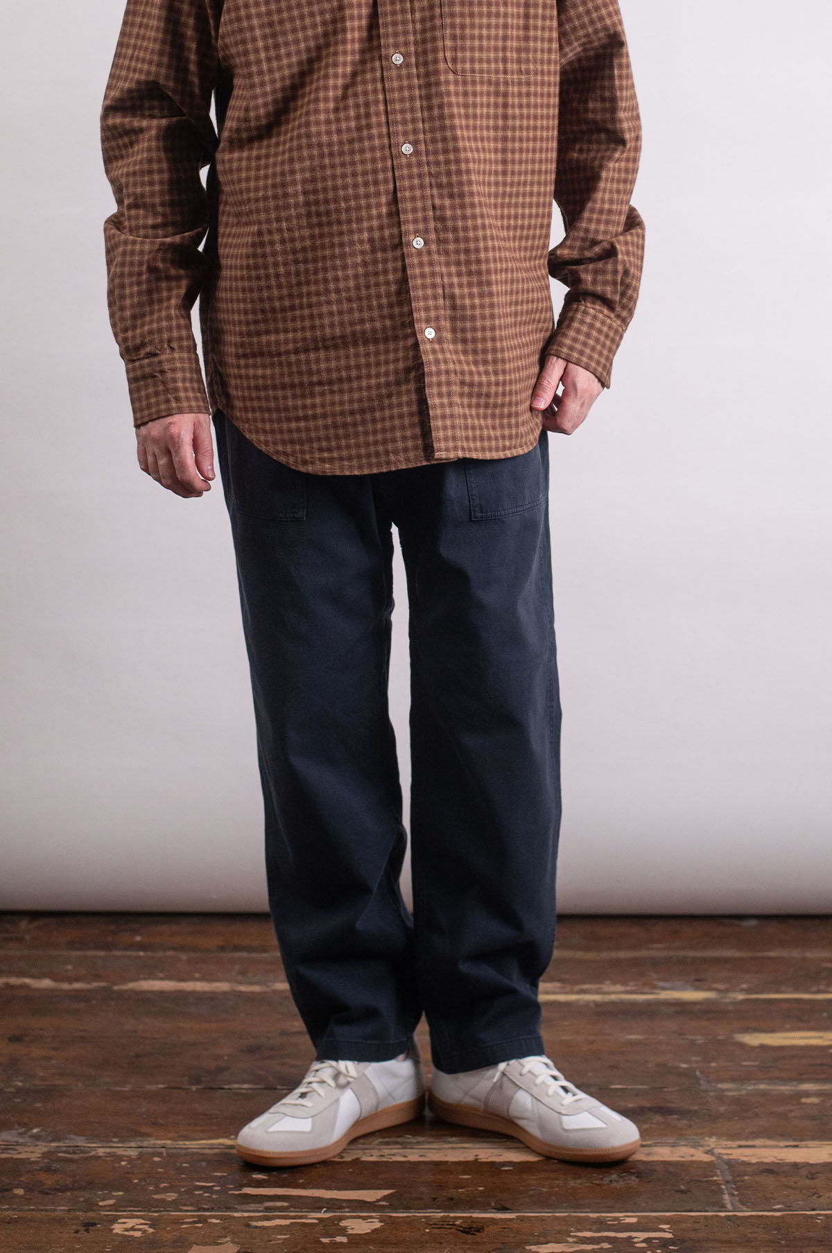 Person wearing a brown checkered shirt, navy pants, and white shoes.