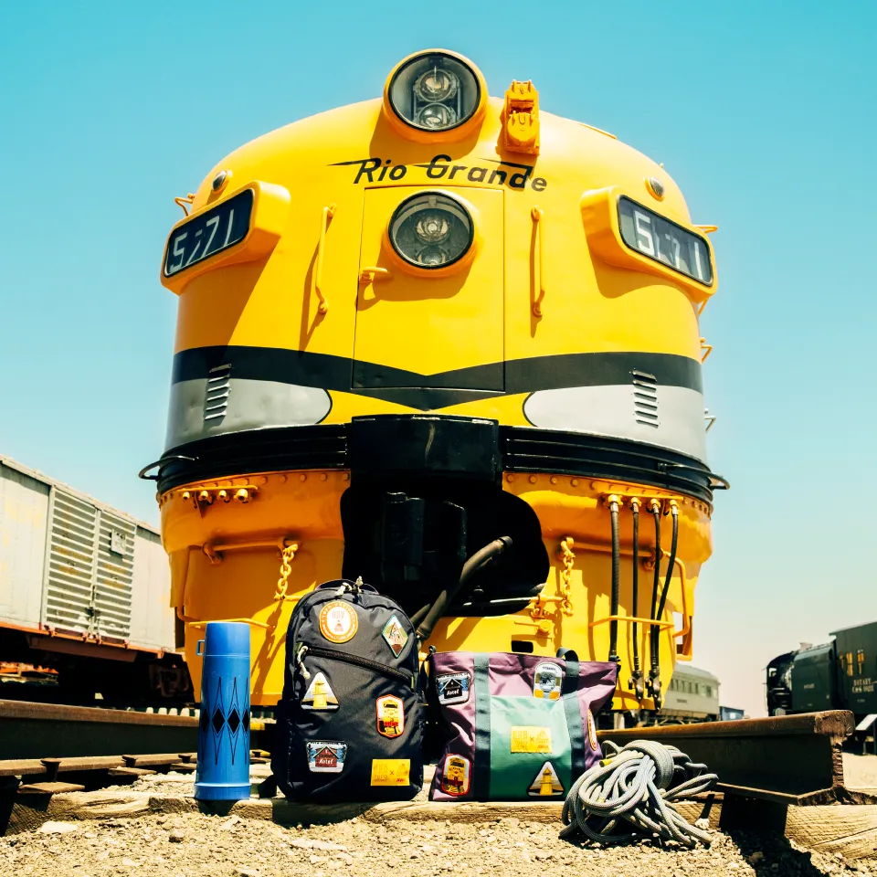 Yellow train engine with backpacks and water bottle in the foreground.