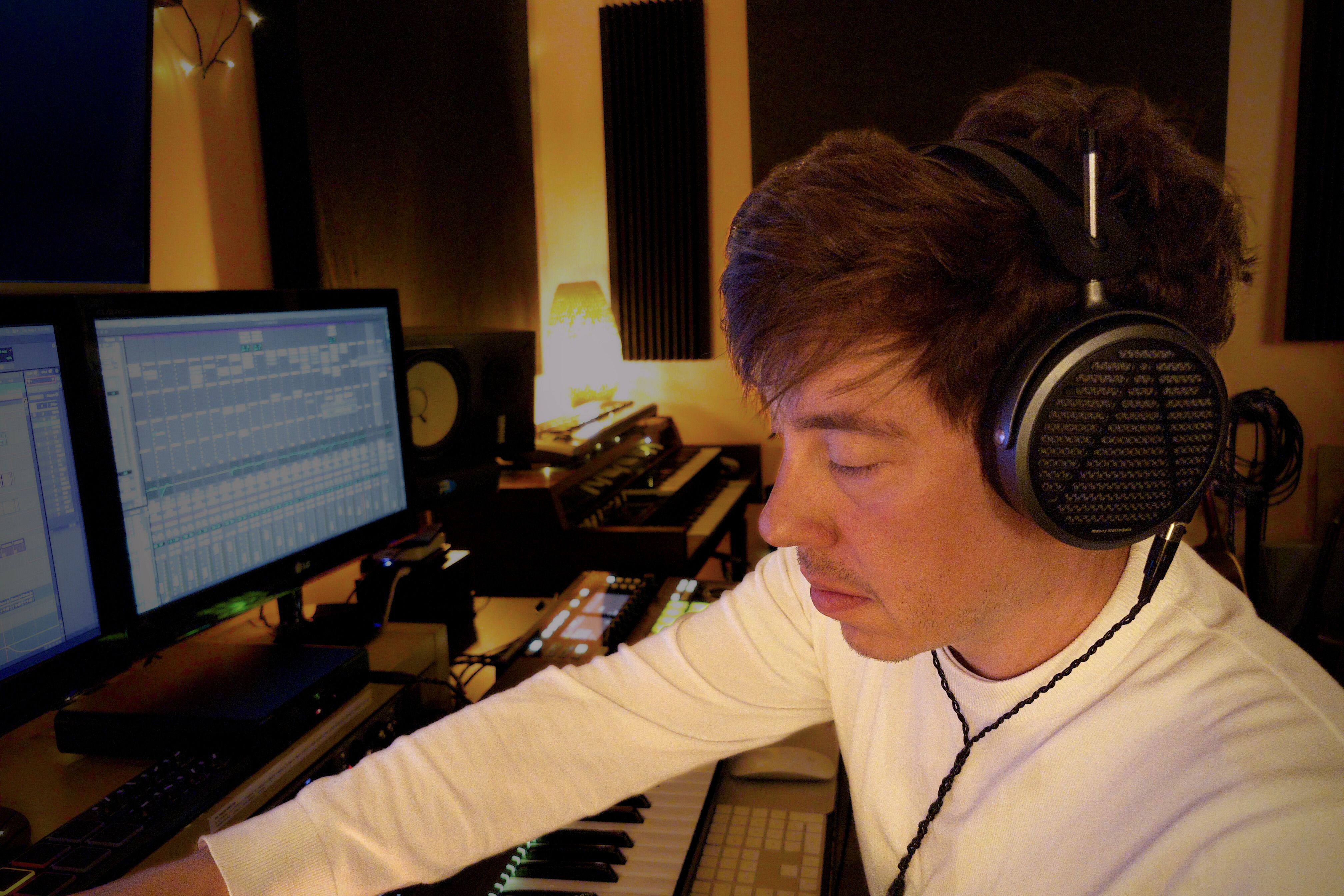 Adam King wearing Audeze MM-500 headphones in a music studio, focused on computer screens.