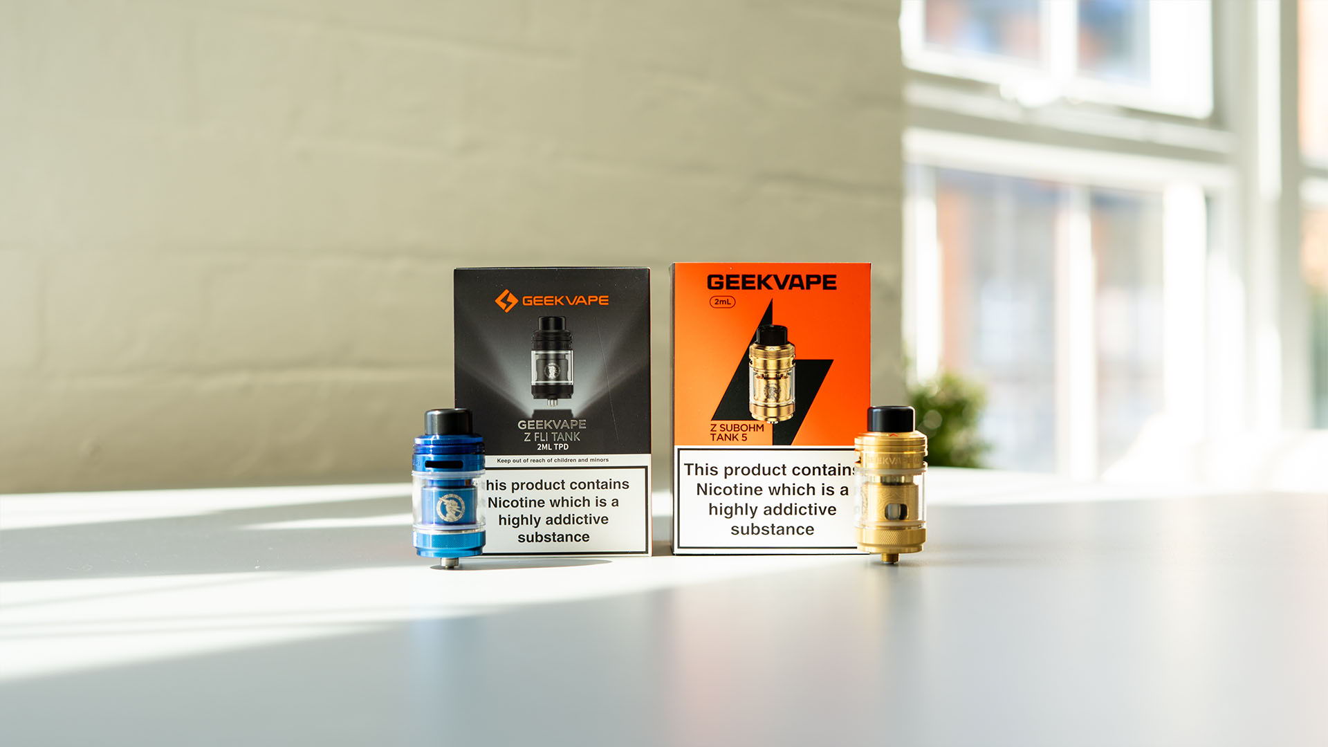 A picture of 2 subohm tanks by Geek Vape sat on a table.
