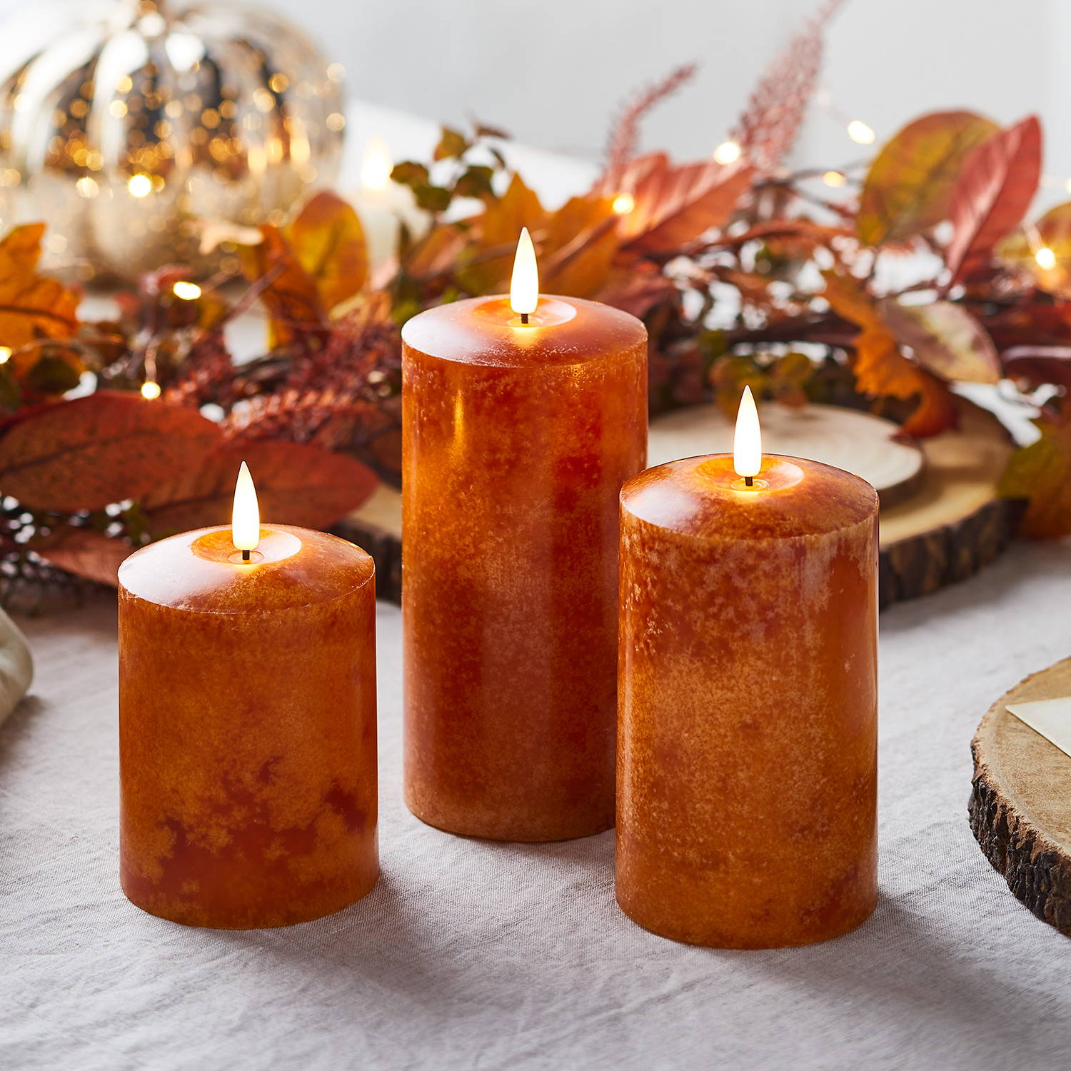 3 orange LED pillar candles on an autumn dining table with autumn foliage in the background.