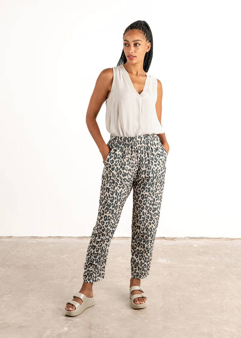 A model wearing a pair of tapered, oatmeal leopard print trousers with a sleeveless off white top and chunky slides