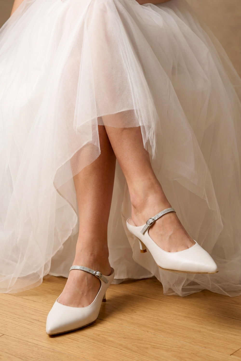 A close-up of a bride's feet in white heels under a tulle wedding dress.