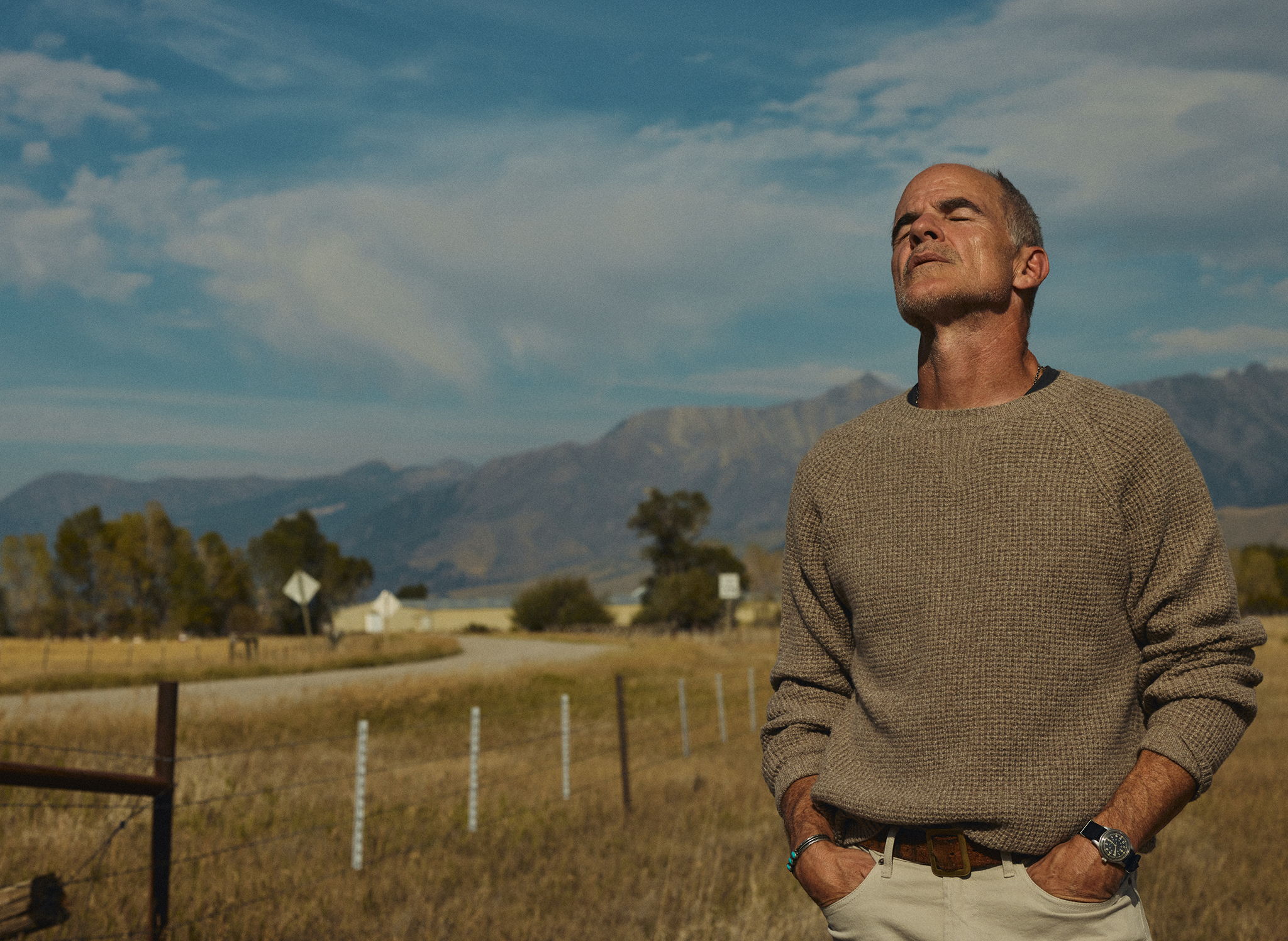 Micheal Kelly looking up at the warm sky wearing the Wade Garment Dyed Five Pocket Pant in Stone Grey and the Sonny Waffle Sweater in Khaki Marl
