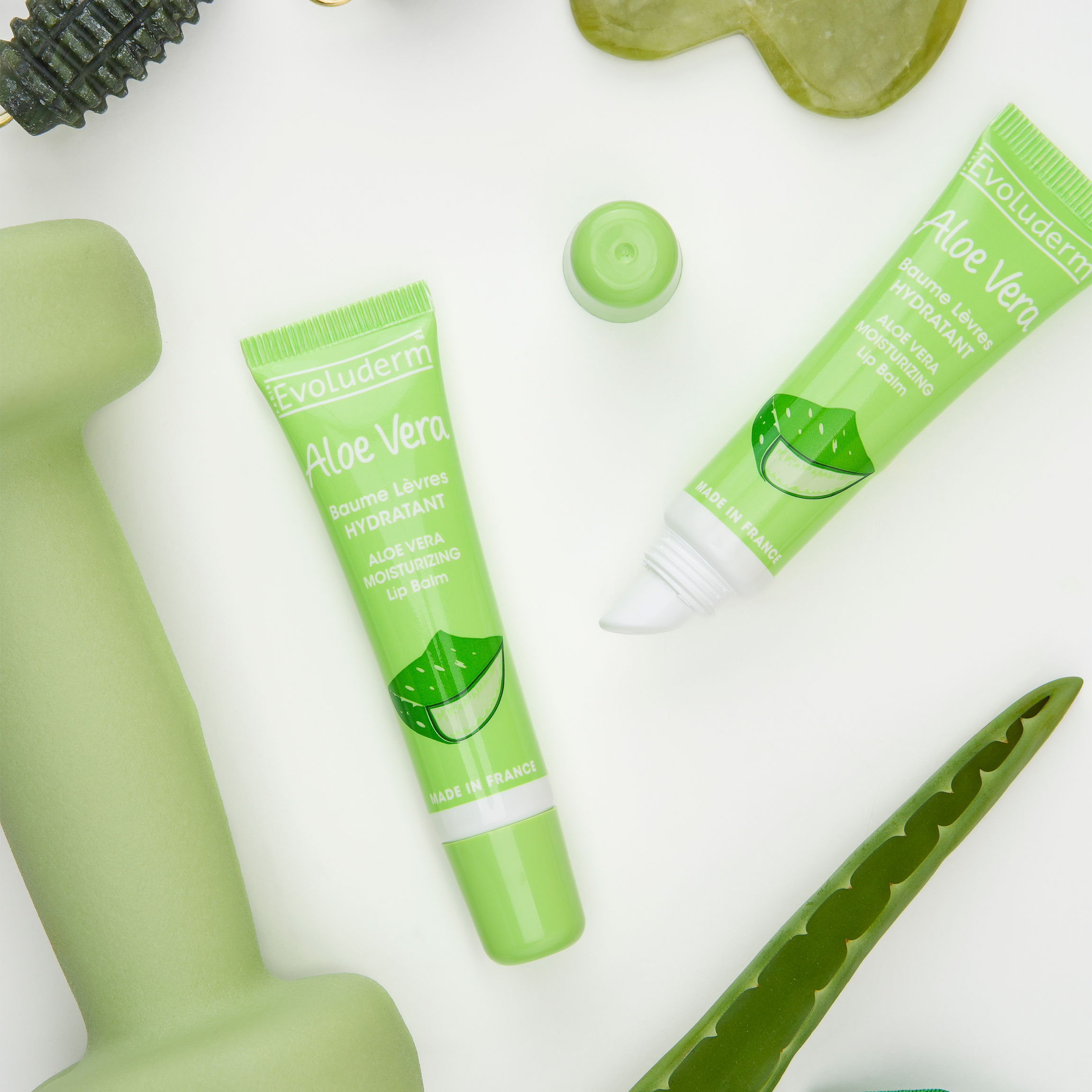 Green skincare products and an aloe vera plant on a white background.