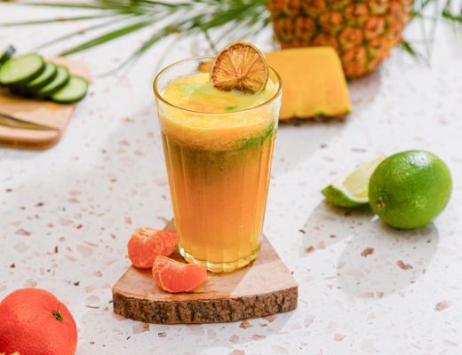 A glass of fruit smoothie with garnish on a wooden coaster.