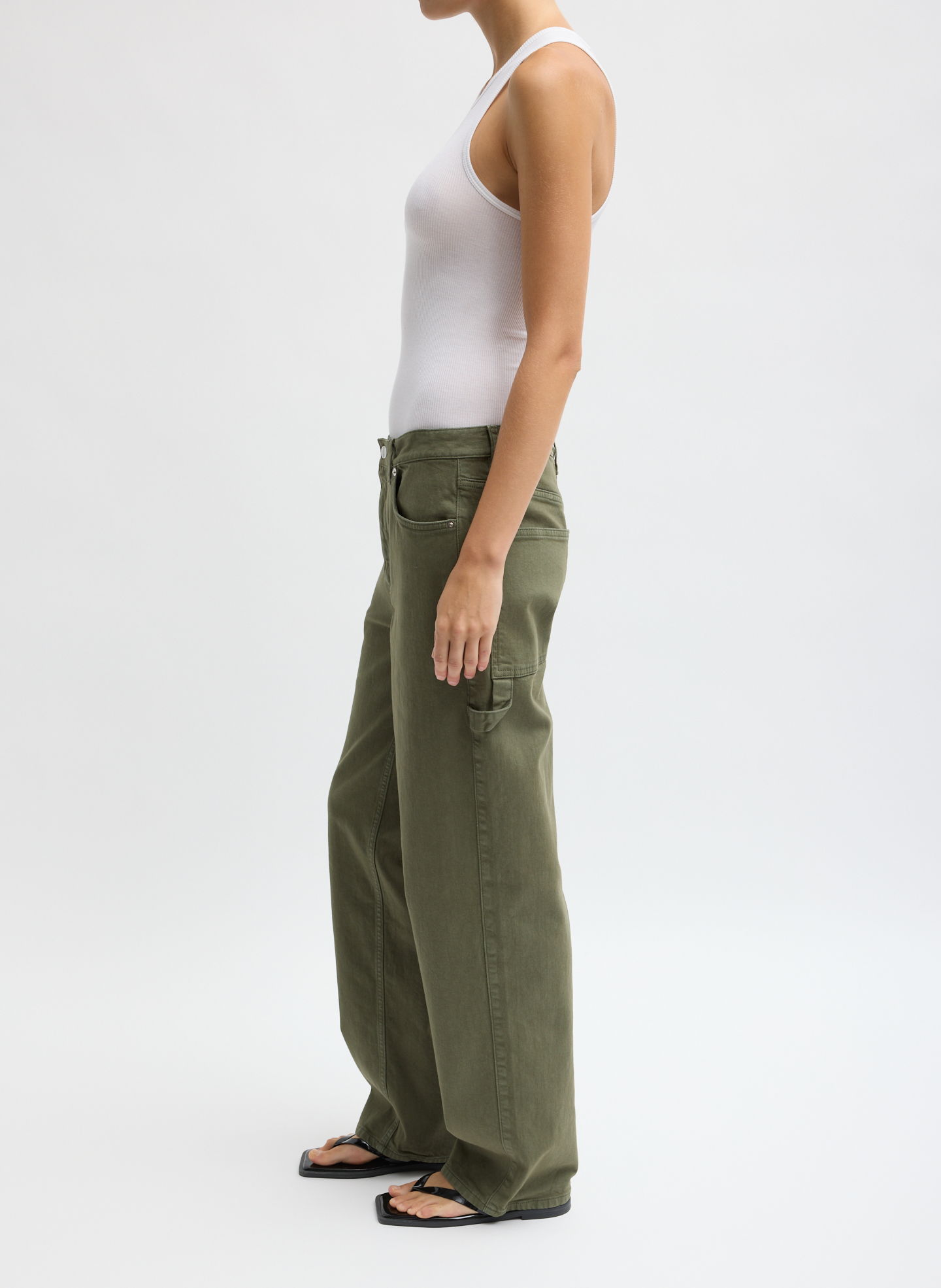 A person wearing a white tank top and green cargo pants, side view.