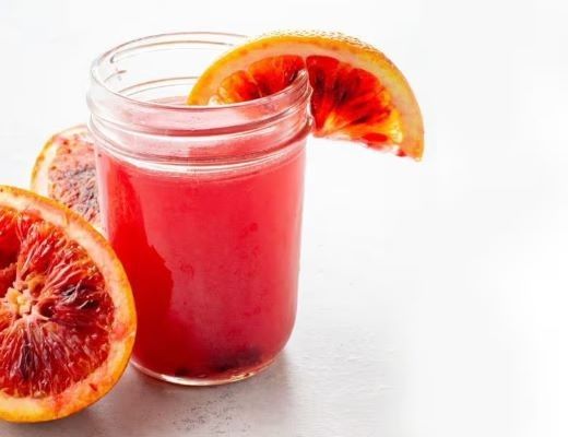 A glass of blood orange juice with a slice of orange.