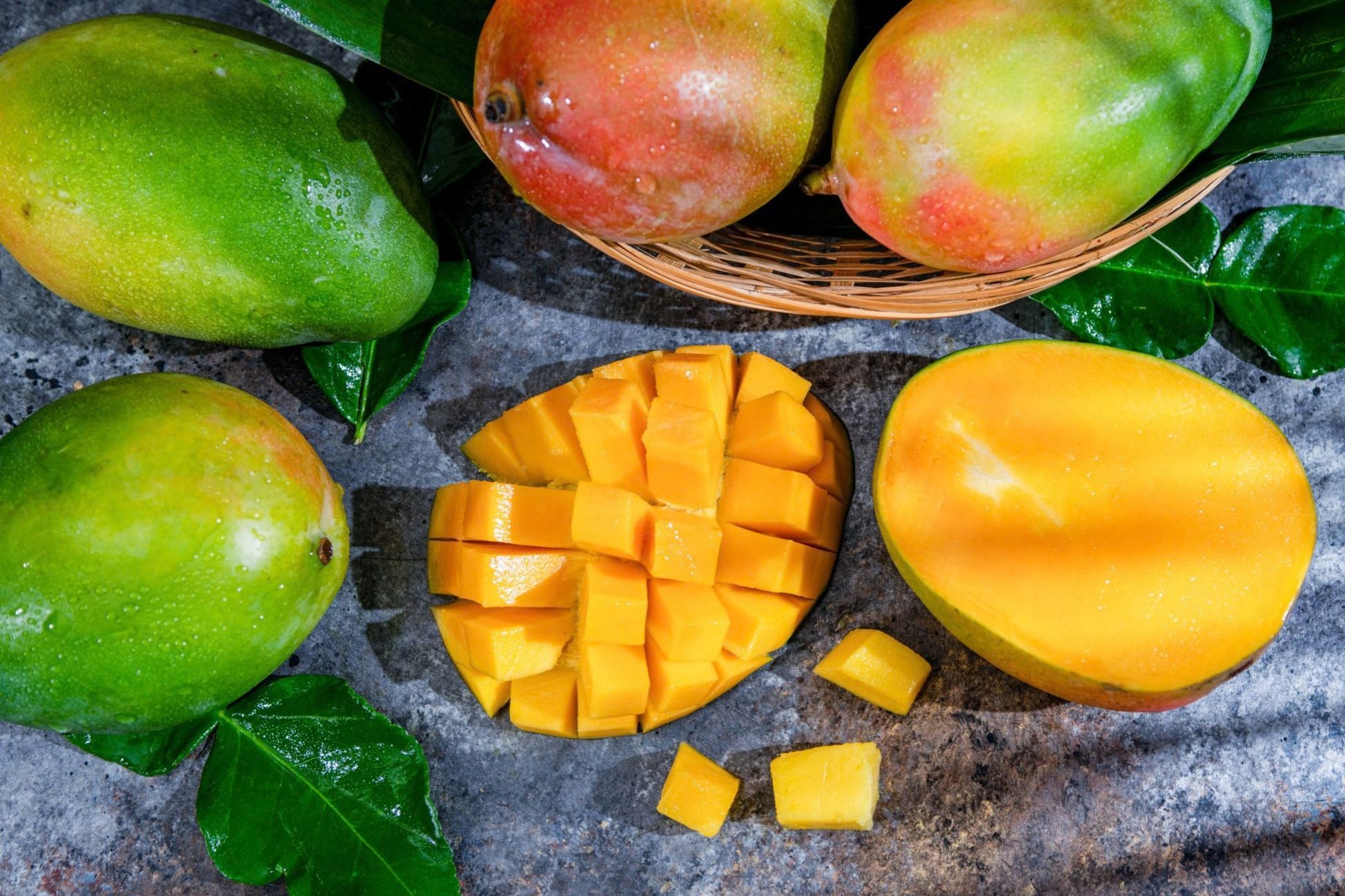 Mangoes with one cut into cubes on a textured surface.