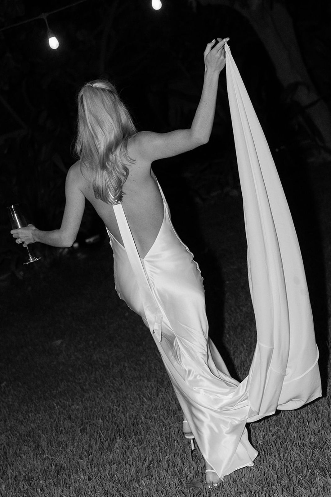 Woman in a backless white dress holding a drink and walking away.