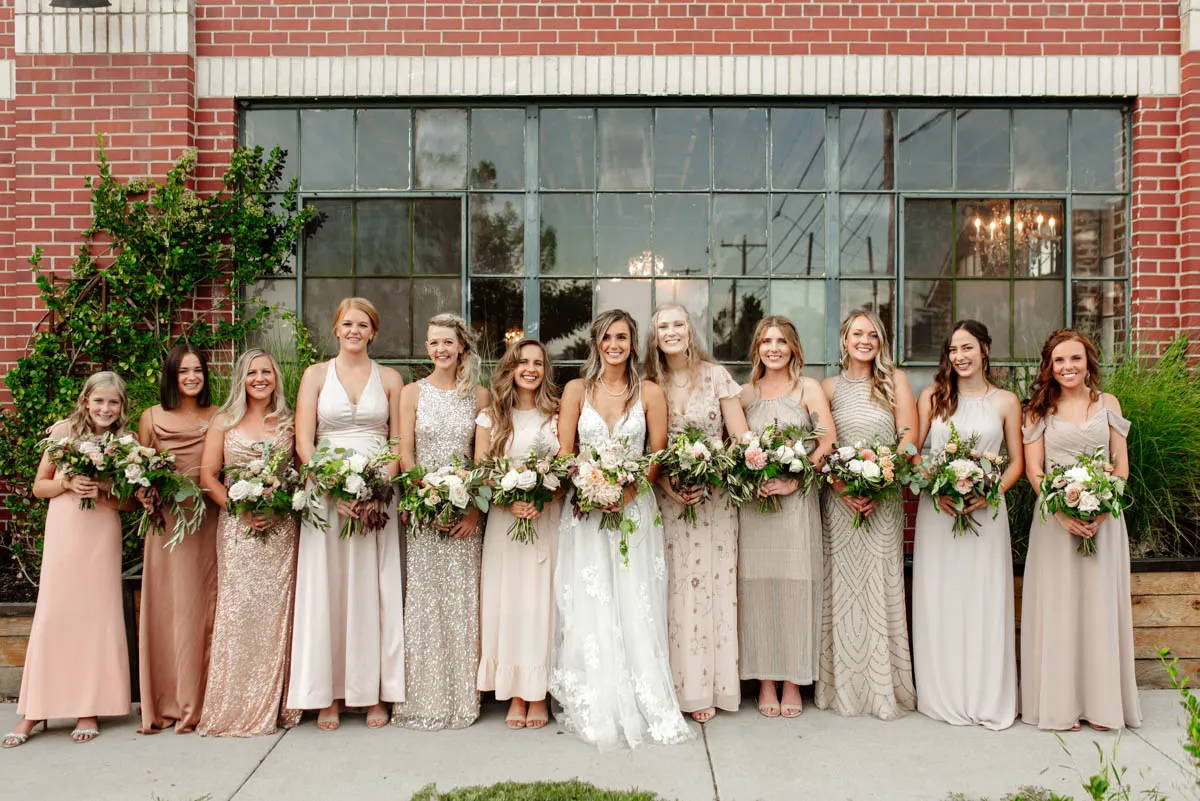 Bride and bridesmaids holding bouquet of flowers in neutral toned dresses