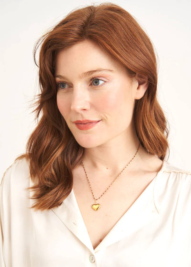 A model wearing a necklace with a golden heart shaped pendant and colourful striped chain