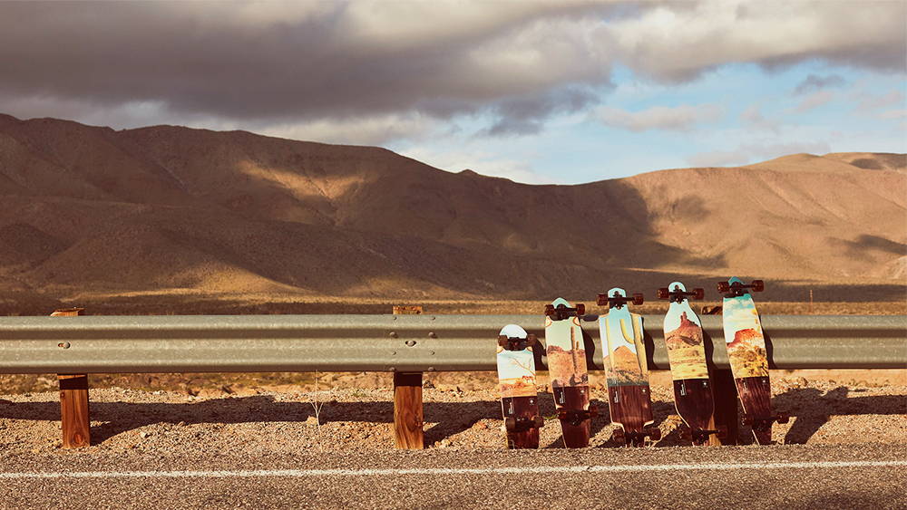 Five skateboards leaning on highway guard rail in front of mountain