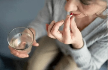 Person taking a pill with a glass of water.