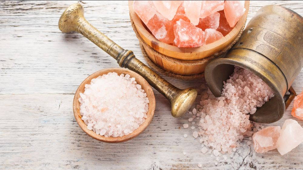 himalayan pink salt in large chunks and granules in an antique metal pestle and motor 