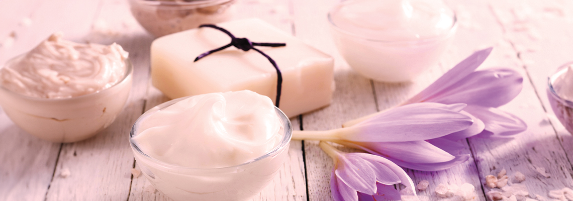 Various skincare products and a purple flower on a wooden surface.